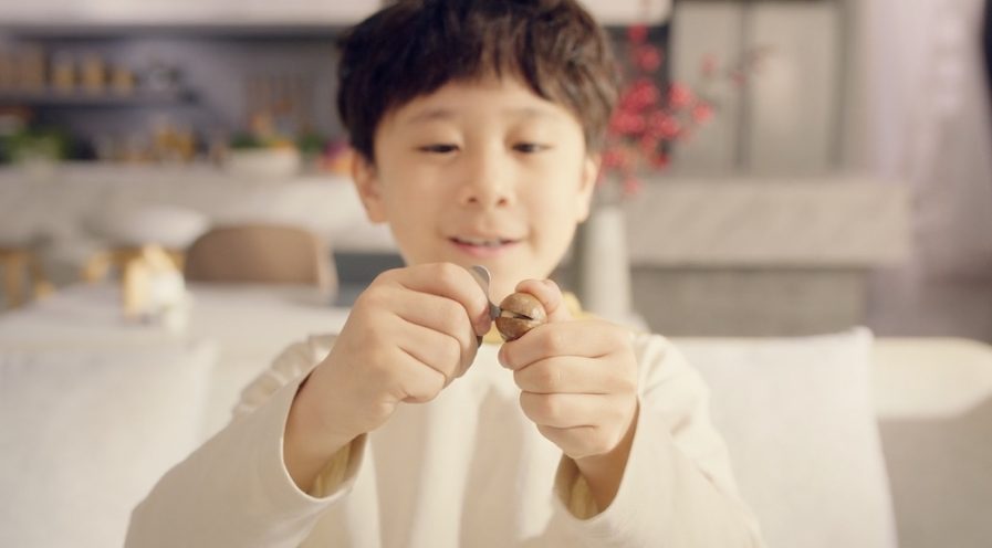 A young Chinese boy cracks open a macadamia shell using a cracking key.