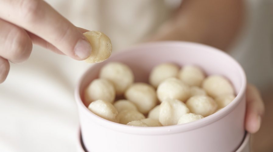 Close up of a person taking a single macadamia from a tin of macadamia nuts